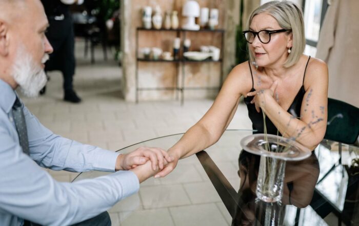 Matrimonio de edad madura cogido de la mano en una mesa, hablando sobre su testamento