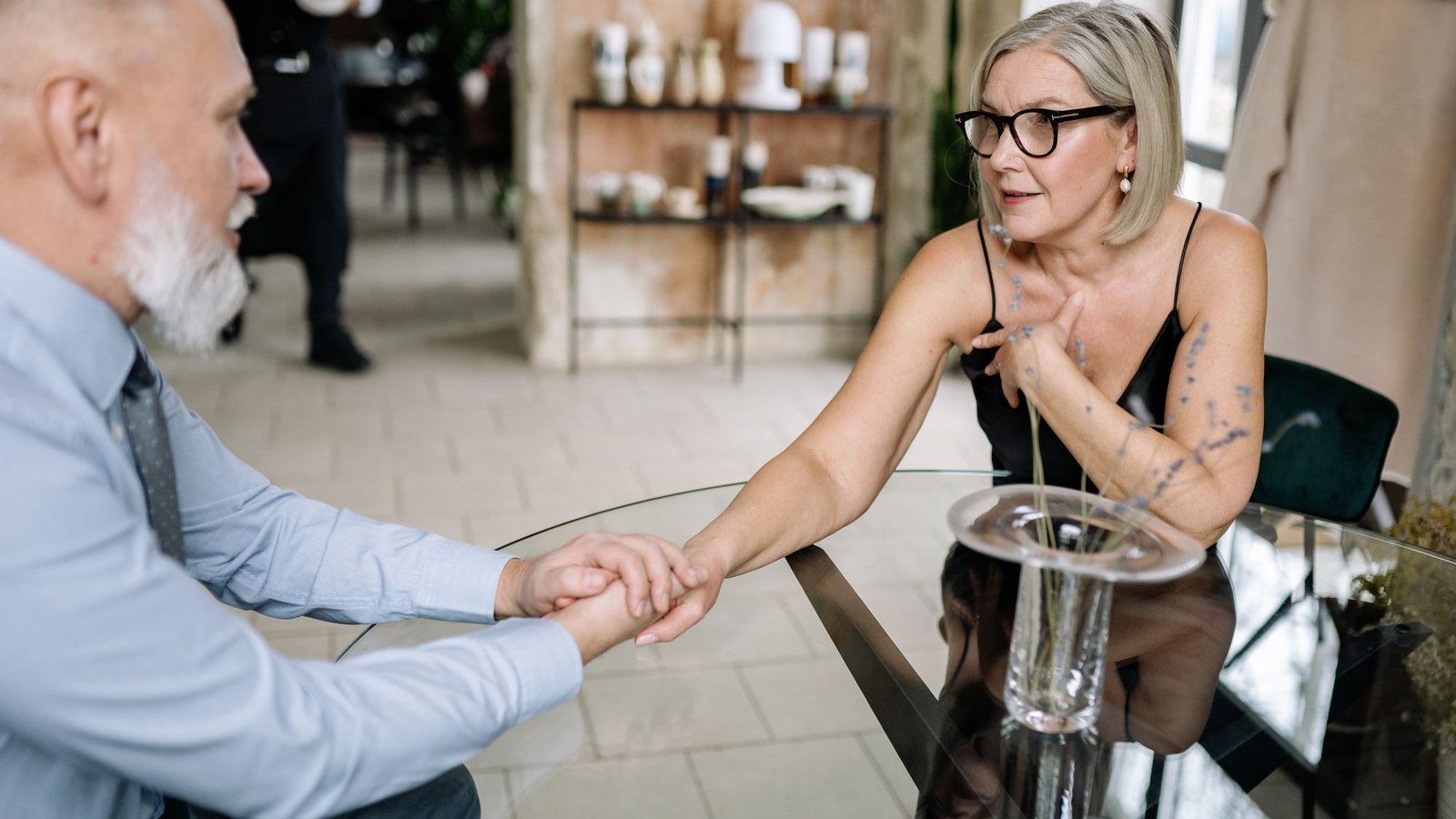Matrimonio de edad madura cogido de la mano en una mesa, hablando sobre su testamento